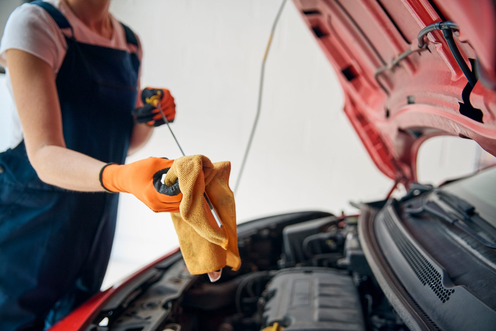 Close Up Of Female Car Auto Mechanic Looking Under Bonnet Of Car Checking Oil Level With Dipstick