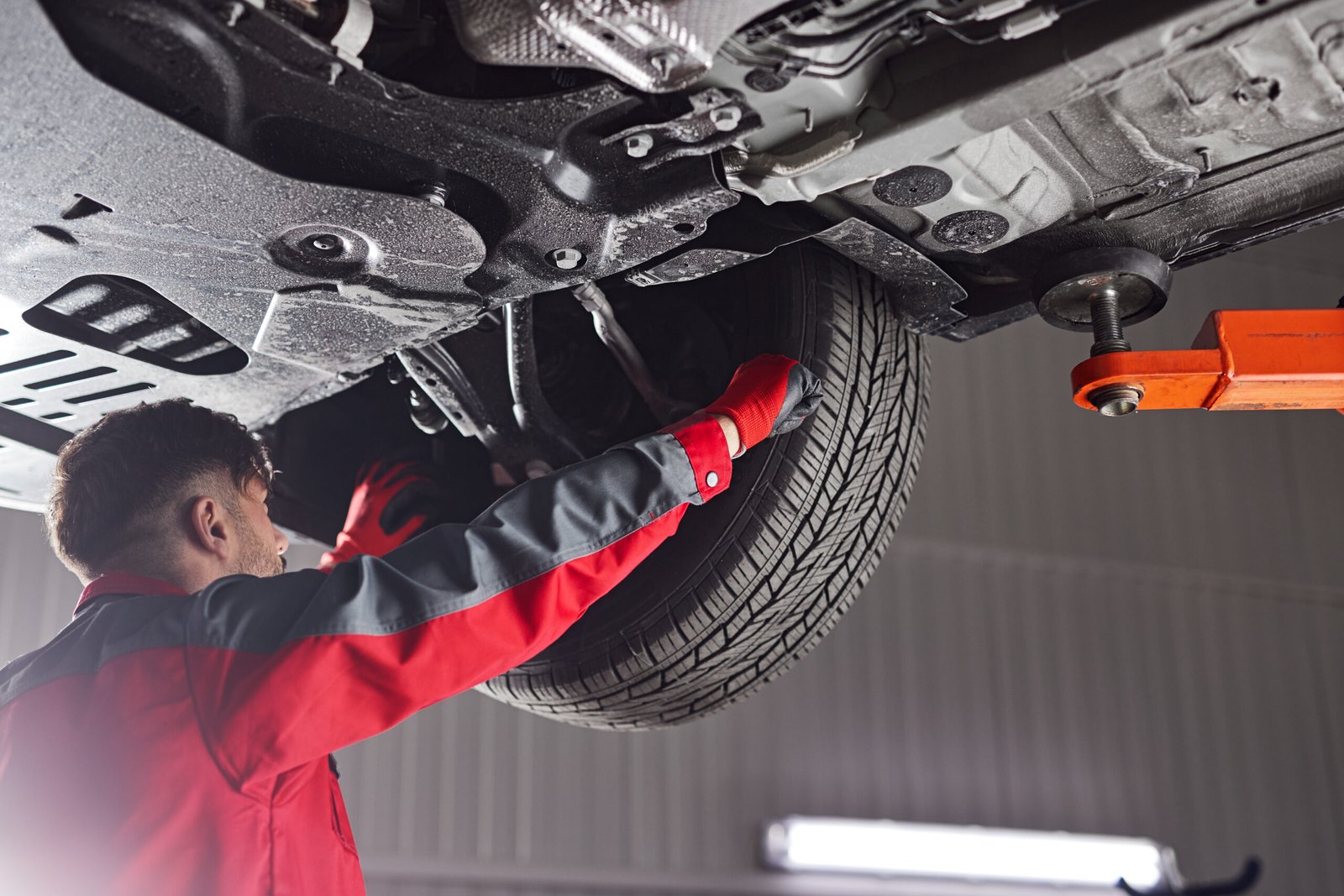 From below man in uniform repairing wheel of vehicle while working in garage